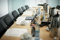 Konferenzraum-Tisch mit Laptop, Dokumenten, Getränken und Kaffeetassen.